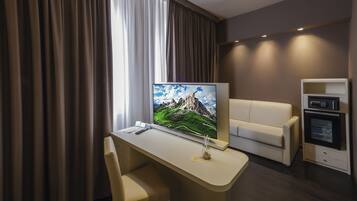 Une chambre d’hôtel moderne dotée d’un grand téléviseur à écran plat, d’un canapé, d’un bureau avec une chaise et d’appareils électroménagers intégrés.