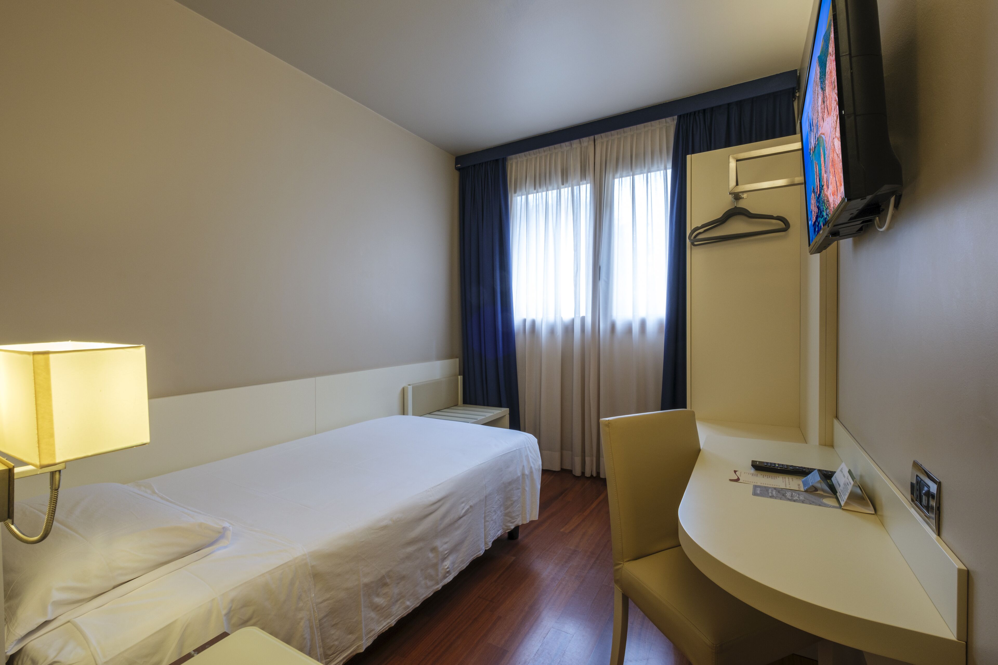 Camera d'albergo con letto, comodino, sedia, scrivania, televisore e tende.