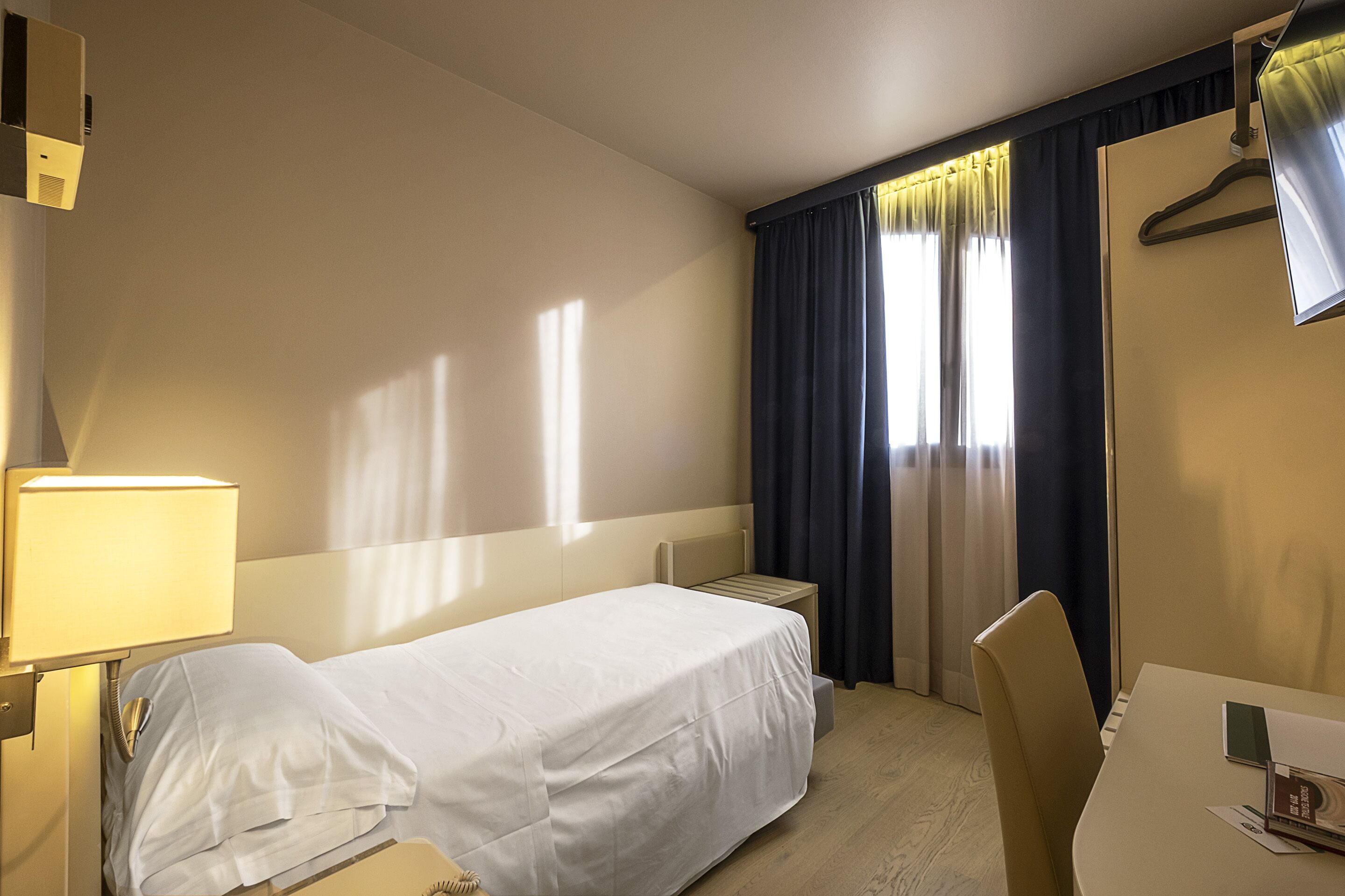 A hotel room with two single beds, a desk, a chair, a lamp, and a TV.