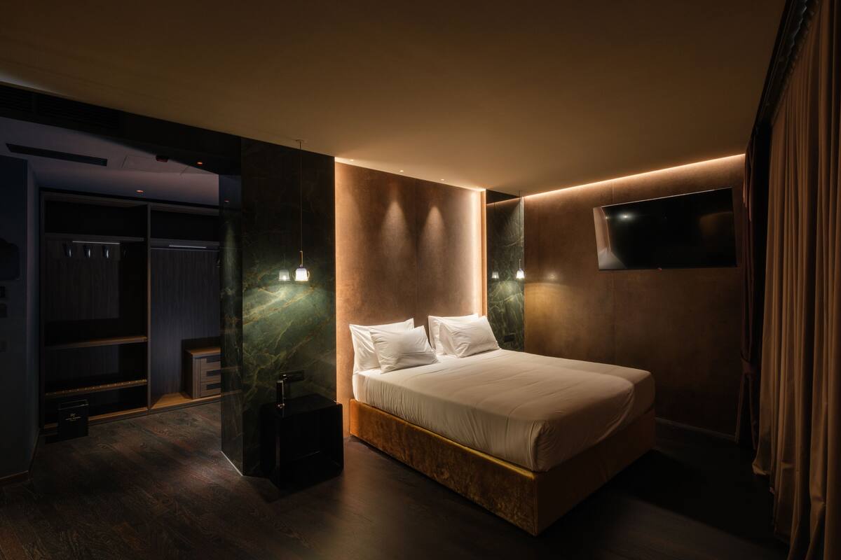 A modern bedroom with a large bed, built-in wardrobe, and a flat-screen TV mounted on the wall.