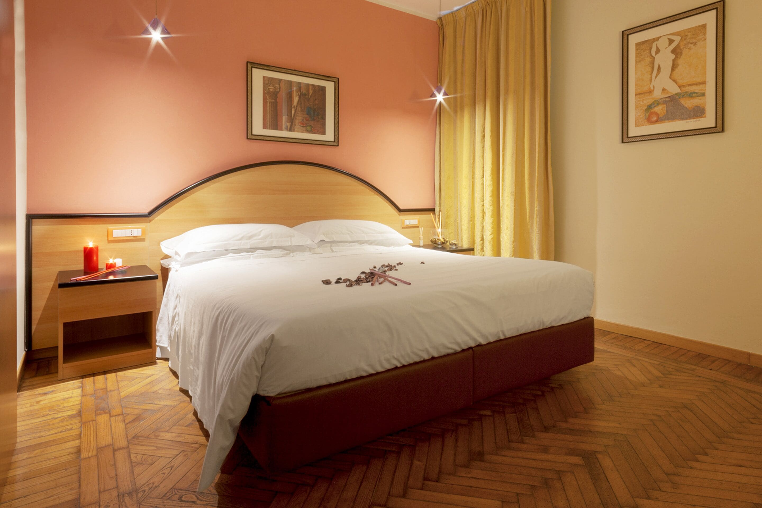 A neatly made bed with white linens, a wooden headboard, and a herringbone-patterned wooden floor.