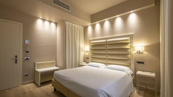 A modern hotel room with a large bed, bedside tables, a built-in bench, and a wall-mounted TV.
