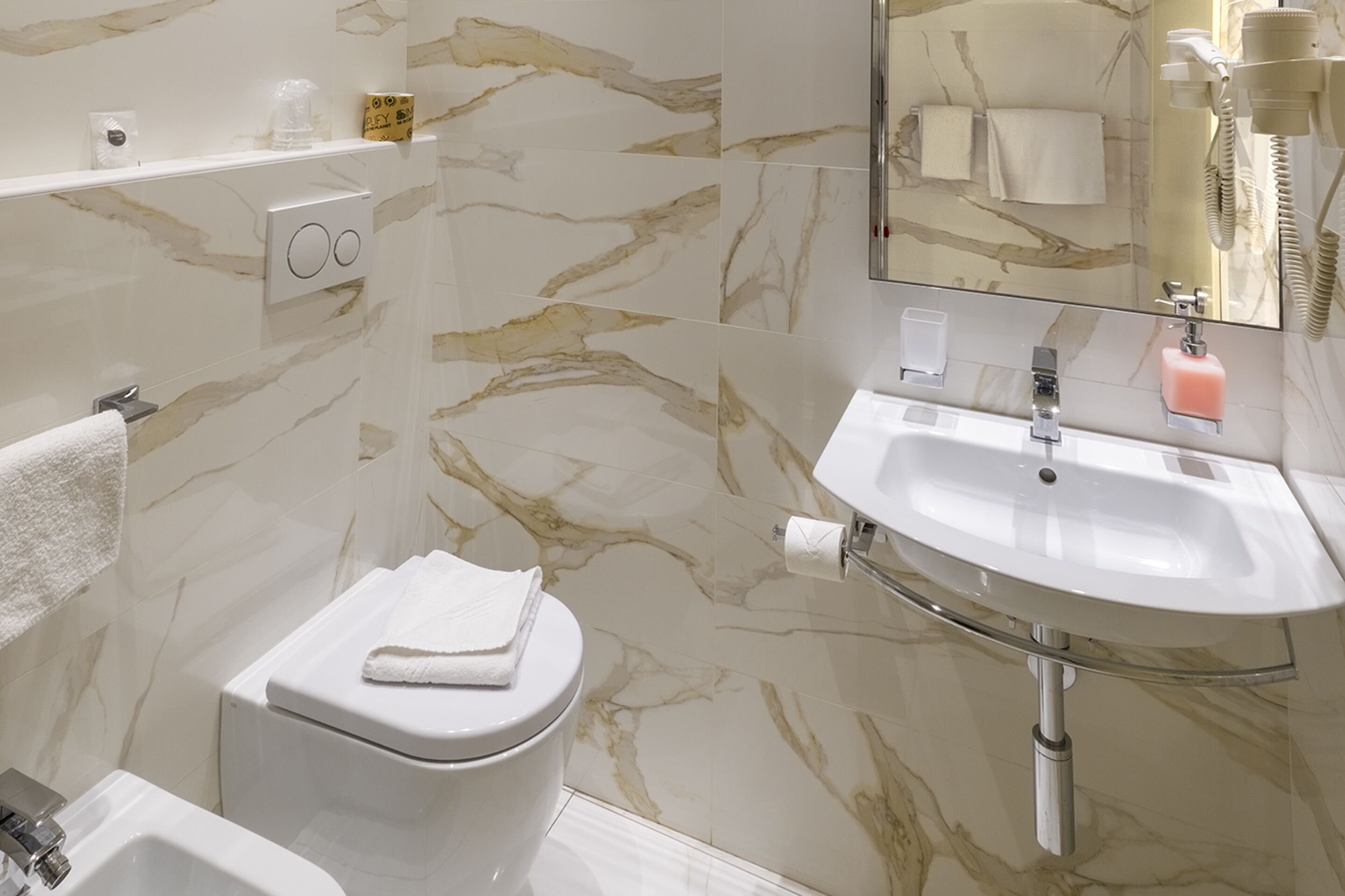 Un baño con pared de mármol, lavamanos blanco y retrete.