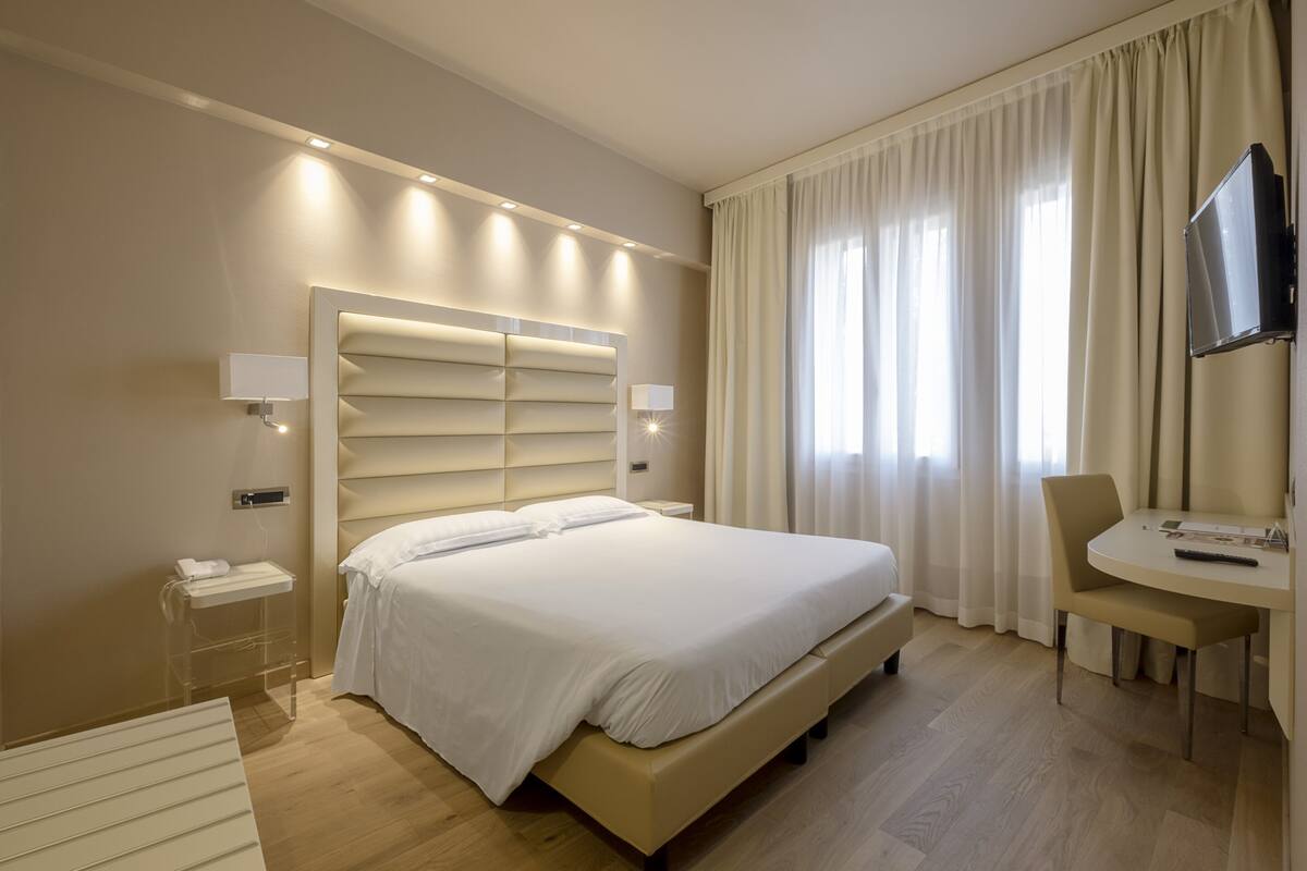 A modern hotel room with a large bed, bedside tables, a desk, and a TV.