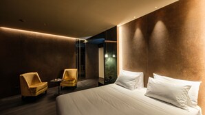 A modern hotel room with a large bed, two armchairs, and a mirror.
