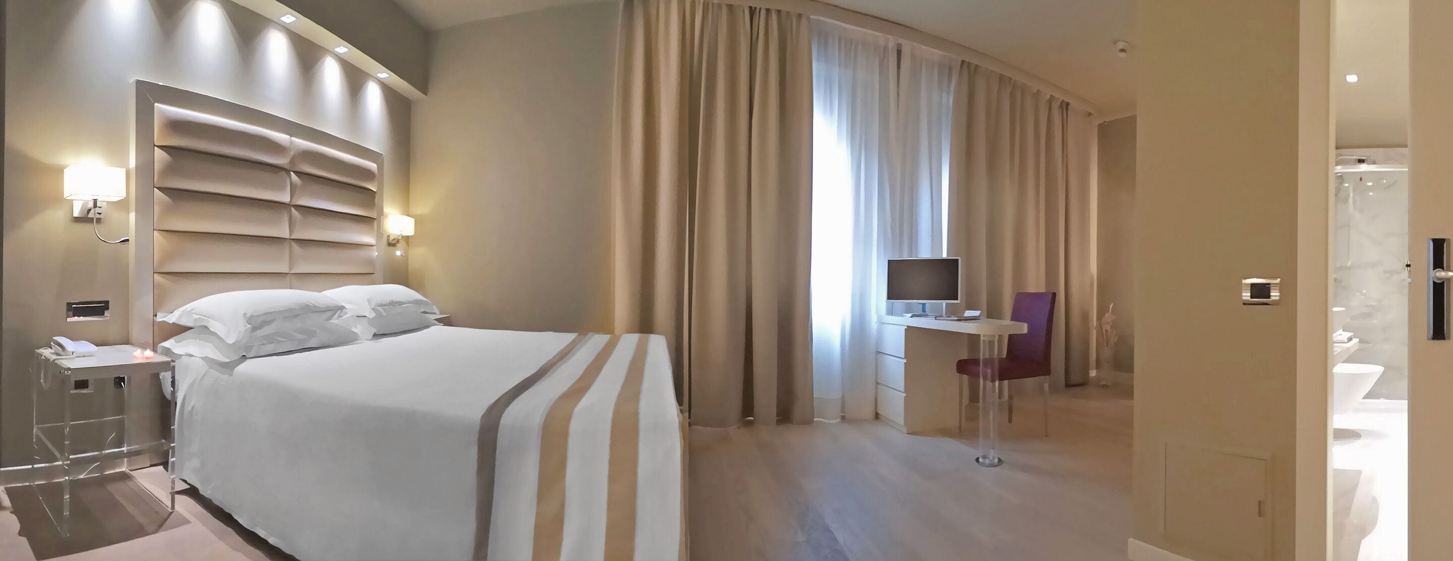 Ein Hotelzimmer mit einem großen Bett, einem Schreibtisch mit Stuhl, einem Fernseher und einem durchgegangenen Badezimmer.