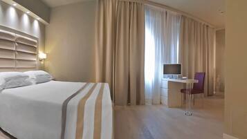 Ein Hotelzimmer mit einem großen Bett, einem Schreibtisch mit Stuhl, einem Fernseher und einem durchgegangenen Badezimmer.
