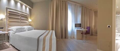 A hotel room with a large bed, a desk with a chair, a television, and a bathroom visible through an open door.