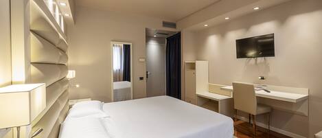 A modern hotel room with a large bed, a desk, a chair, a TV, and a mirror.