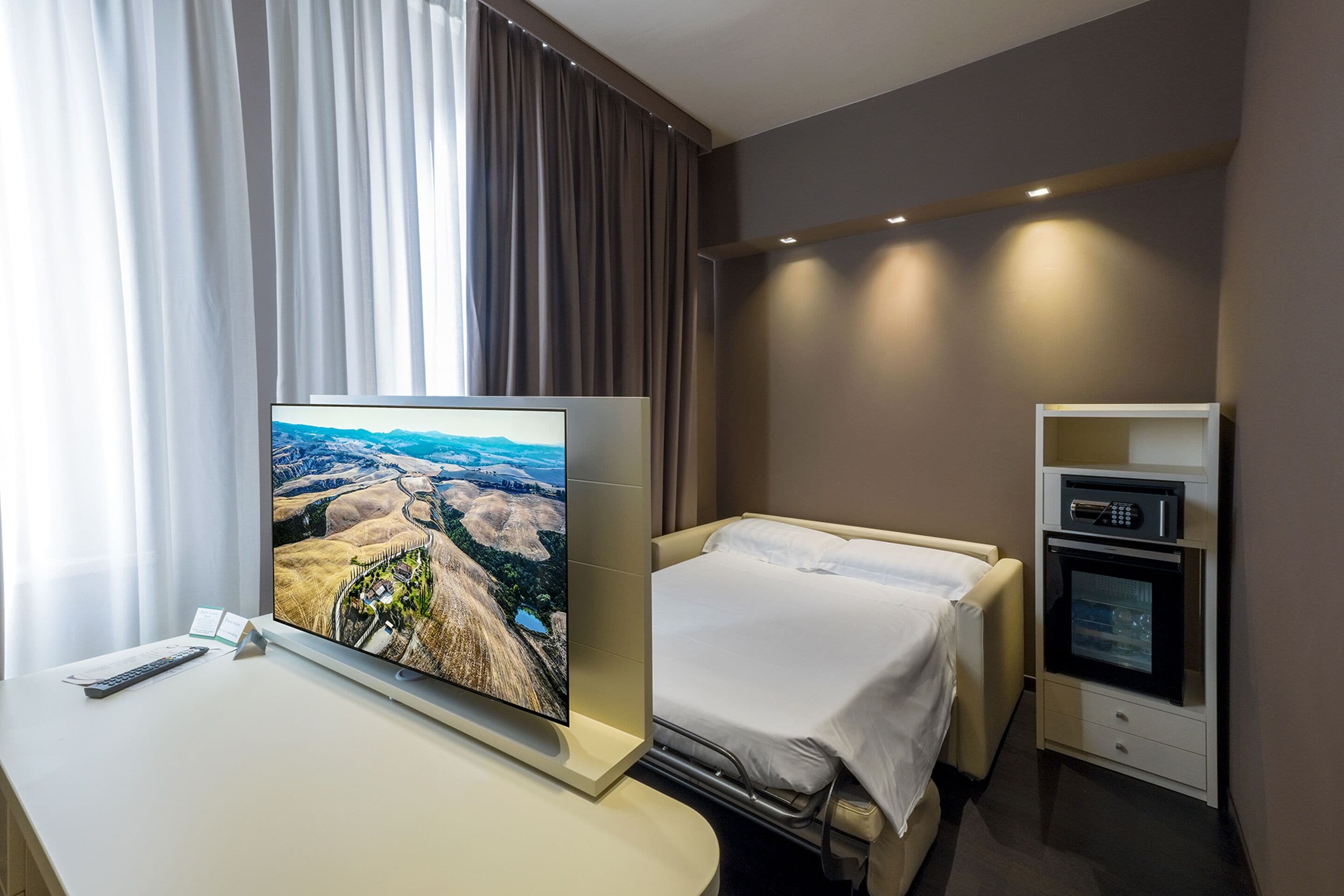 Una habitación de hotel con cama, escritorio con televisor, microondas y un pequeño armario.