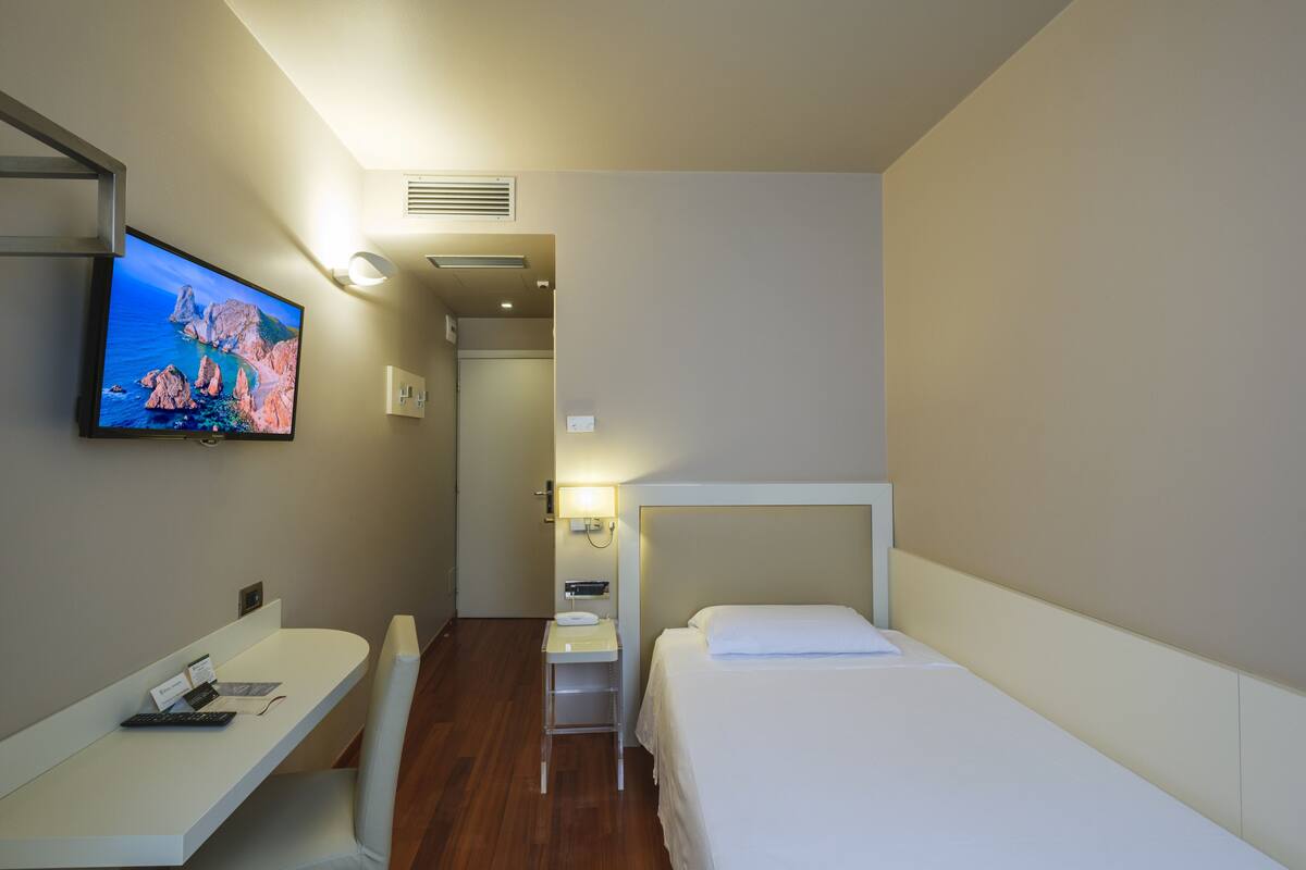 A hotel room with a bed, a desk, a chair, a television, and a bathroom door.