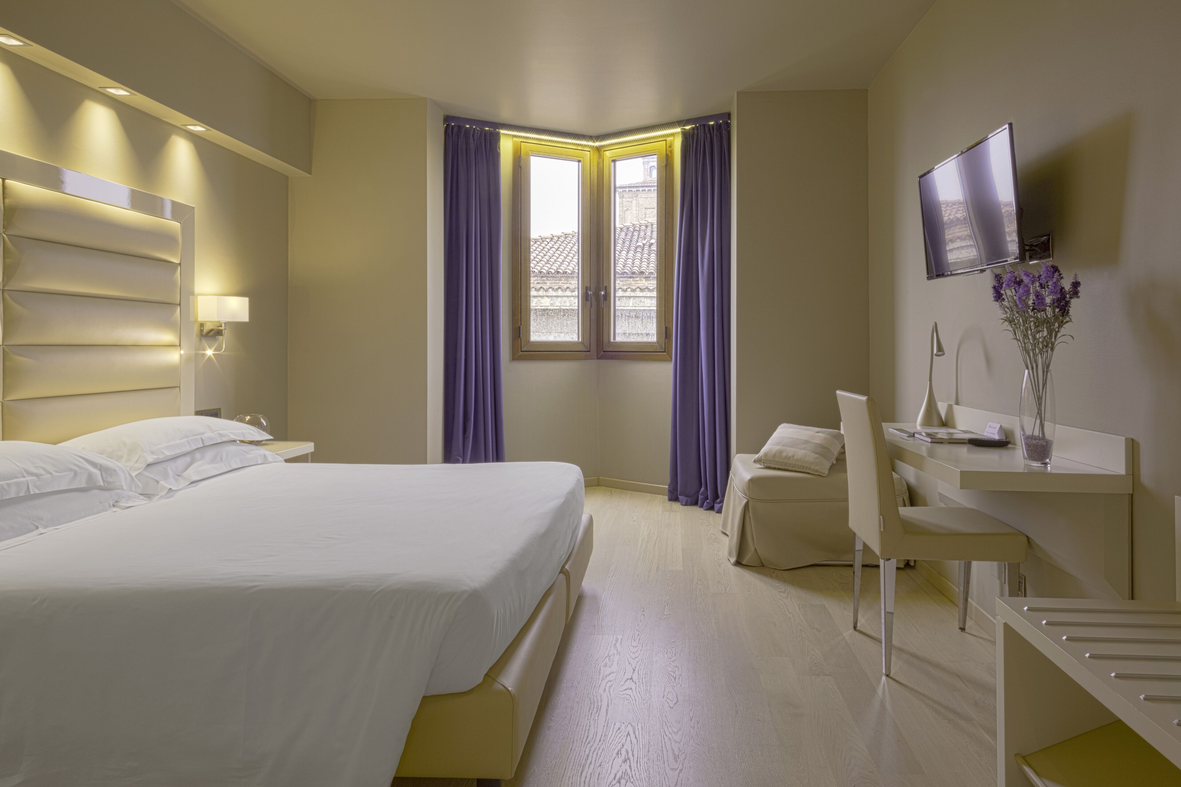 A hotel room with a bed, a desk, a chair, a TV, and a window with curtains.