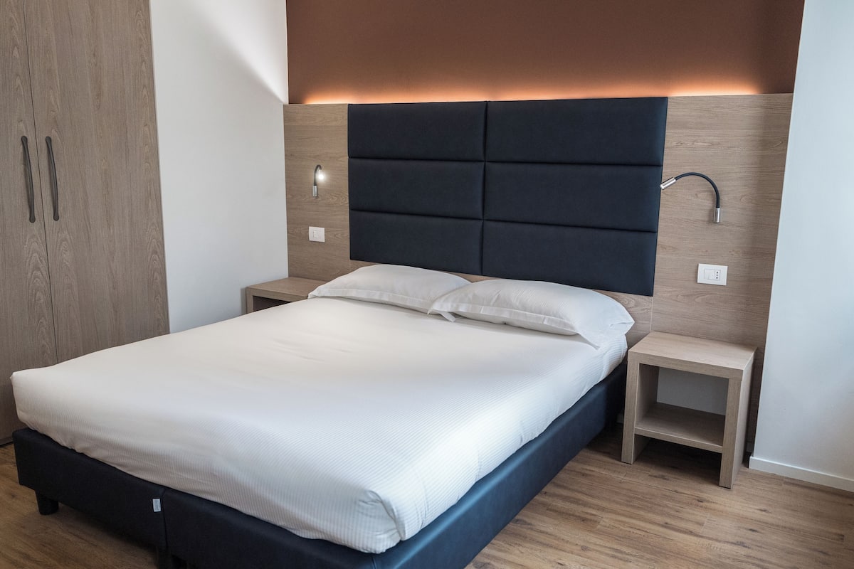 A modern bedroom with a large bed, wooden headboard, bedside tables, and a nightstand.