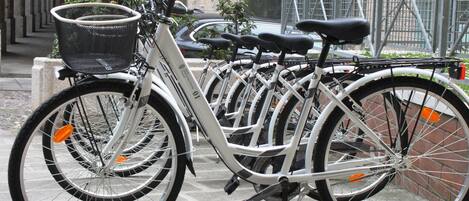 Várias bicicletas estacionadas em área externa, com um muro de pedra e um portão de metal ao fundo.