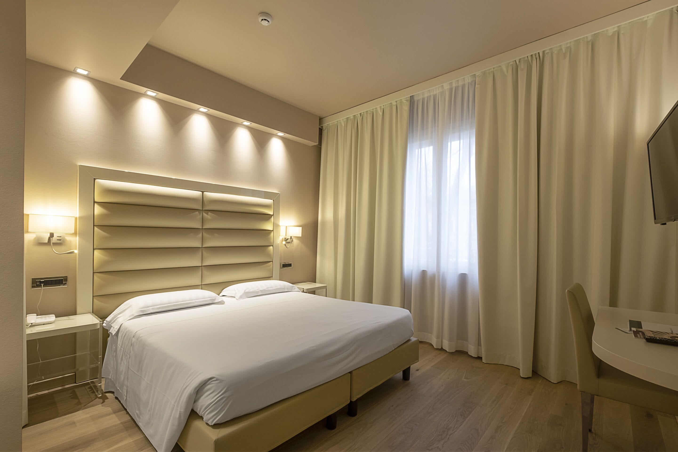 A hotel room with a large bed, bedside tables, a desk, and a TV.