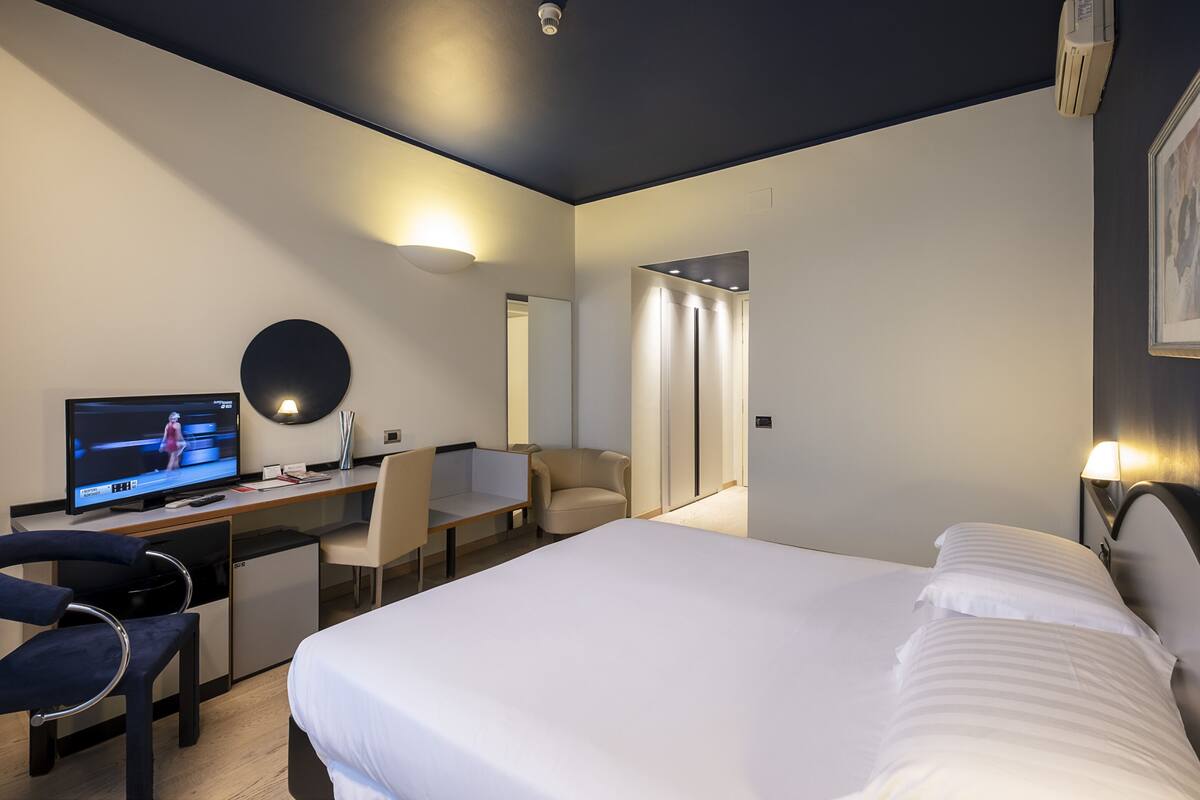 A modern hotel room with a bed, desk, chair, television, and a mirror.