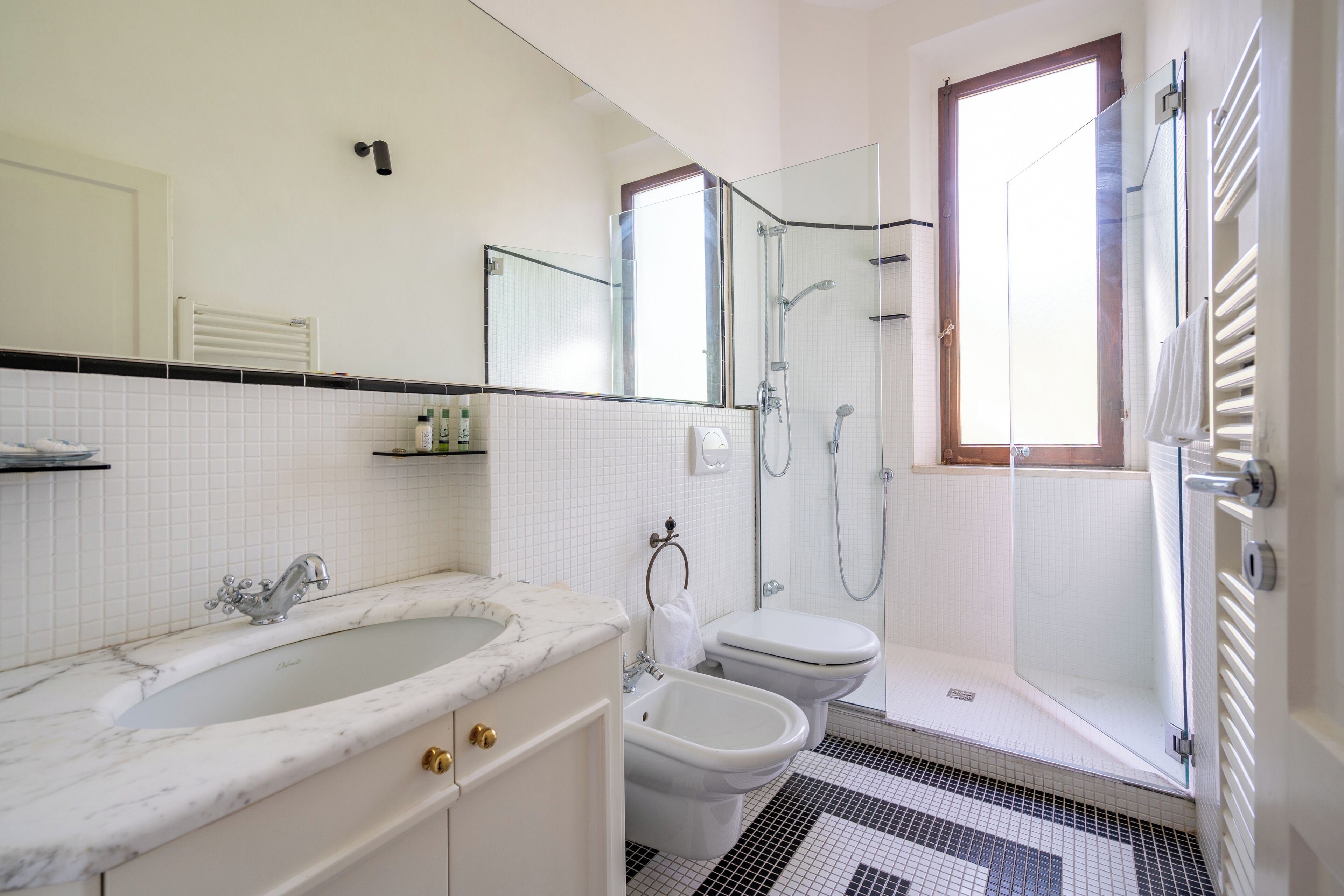 Ein Badezimmer mit Marmorwaschbecken, Toilette, Bidet, einer Duschkabine aus Glas und einem großen Fenster.