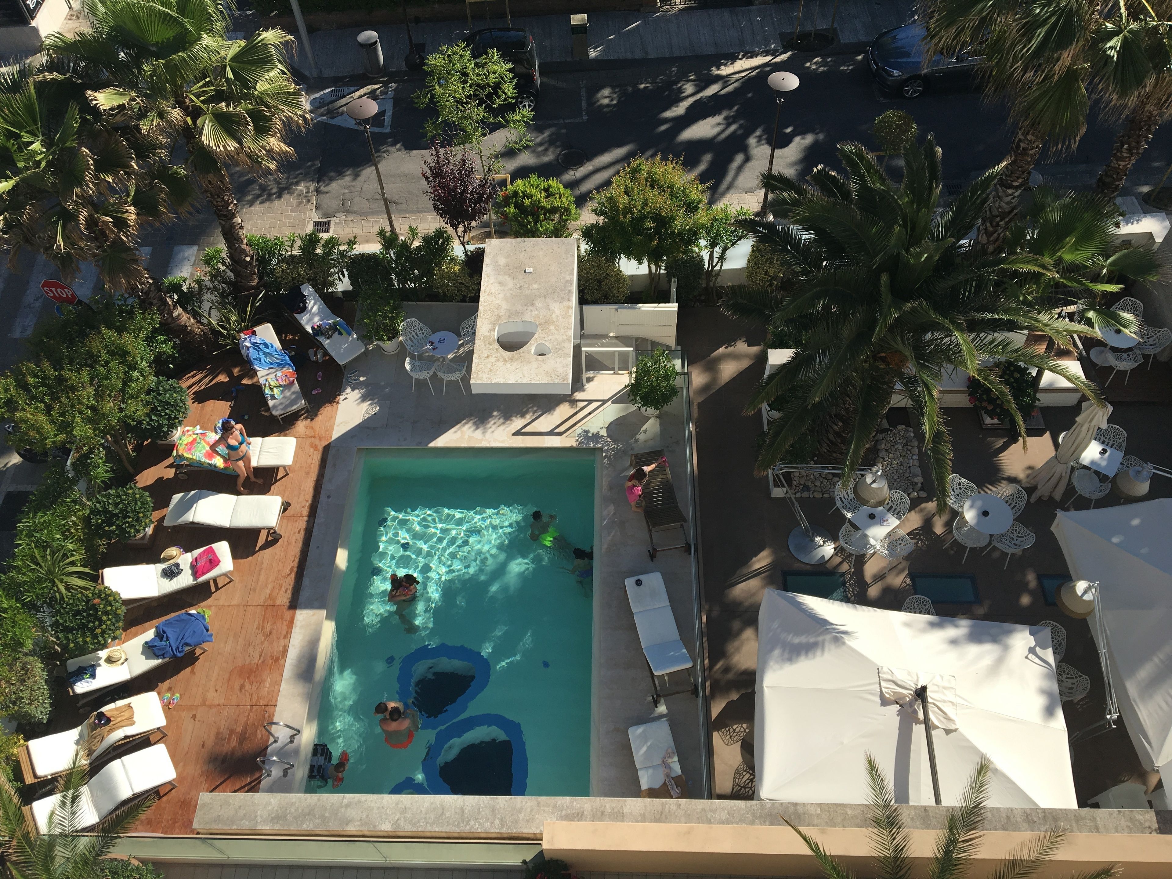 An aerial view of a pool area with lounge chairs, a swimming pool, and palm trees.