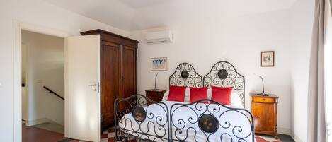 Un dormitorio con piso a cuadros, estructura de cama metálica, armario de madera y mesita de noche con lámpara.