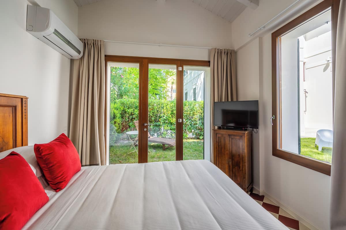 Una habitación de hotel con una cama, un televisor y un ventanal corredera que da a un jardín.