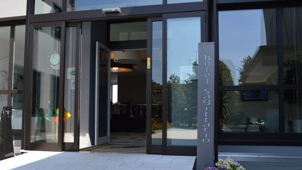 A hotel entrance with glass doors, a sign reading "hotel Sagittario," and a potted plant with flowers in front. - Hotel Sagittario (Padova)