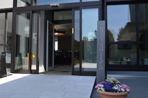 Entrada de un hotel con puertas de cristal, un letrero que dice "hotel Sagittario" y una planta con flores al frente.