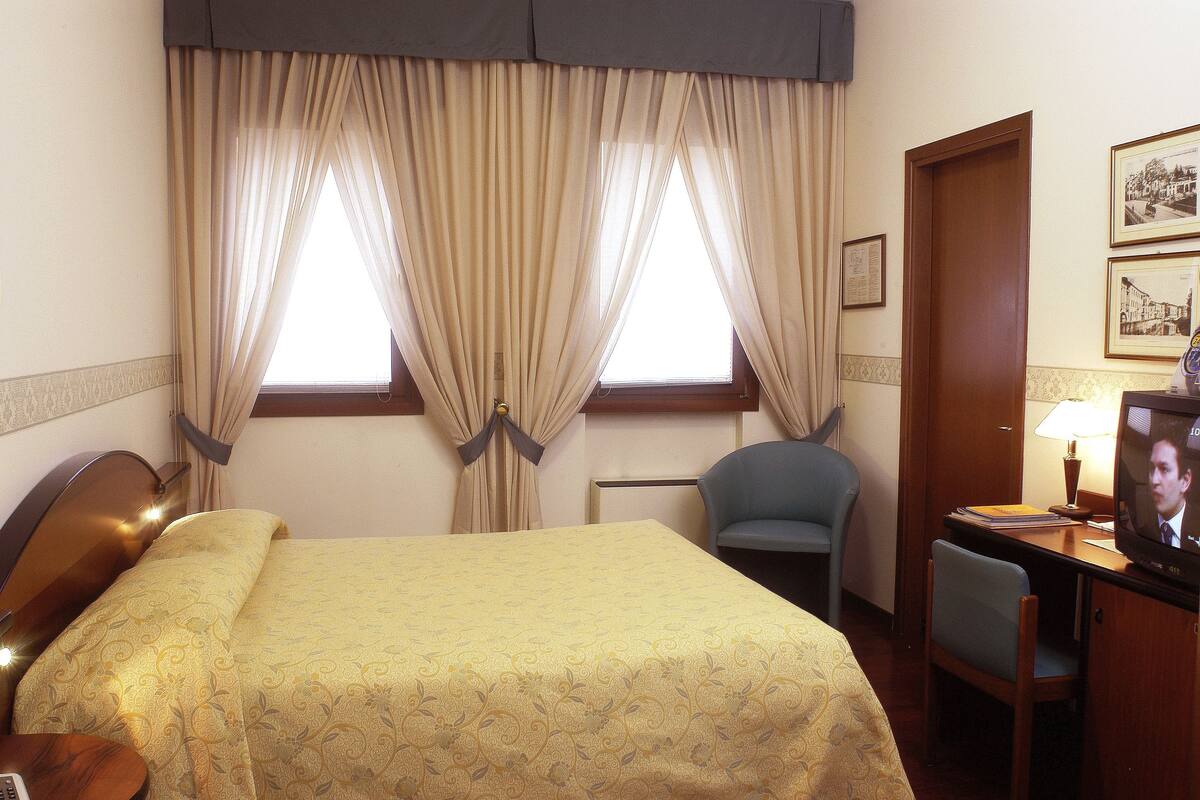 Une chambre d’hôtel avec un lit, un bureau avec une télévision, une chaise et des rideaux.
