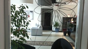 A modern living room with a large black sofa, a wooden coffee table with magazines, and a large black planter with green leaves. - Hotel Sagittario (Padova)