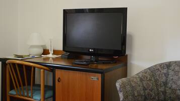 Una habitación de hotel con un escritorio de madera, un televisor, una lámpara y un sillón estampado.