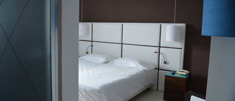 Una habitación de hotel moderna con una cama grande, lámparas de noche, una mesita de madera y una silla.