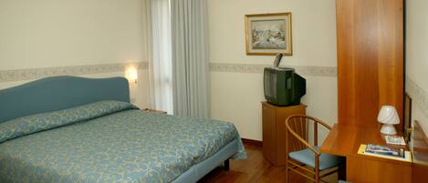 Una habitación de hotel con cama, escritorio, silla, televisor y un cuadro en la pared.