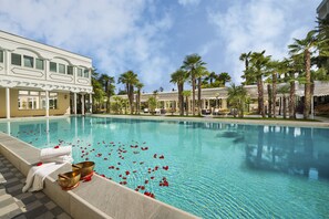 A swimming pool with a clear blue water, surrounded by palm trees and a building with a white facade. - HOTEL TERME METROPOLE – ORIENTAL SPA & RESORT (Abano Terme)