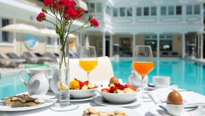 A breakfast setting with fruit, pastries, and beverages by a poolside, overlooking a resort building. - HOTEL TERME METROPOLE – ORIENTAL SPA & RESORT (Abano Terme)