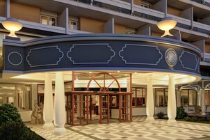 Entrada de un hotel con suelo a cuadros, un arco central y un balcón con barandillas.