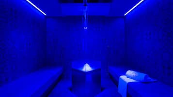 Una stanza con una struttura metallica centrale, due panche, pareti decorate e illuminazione blu.