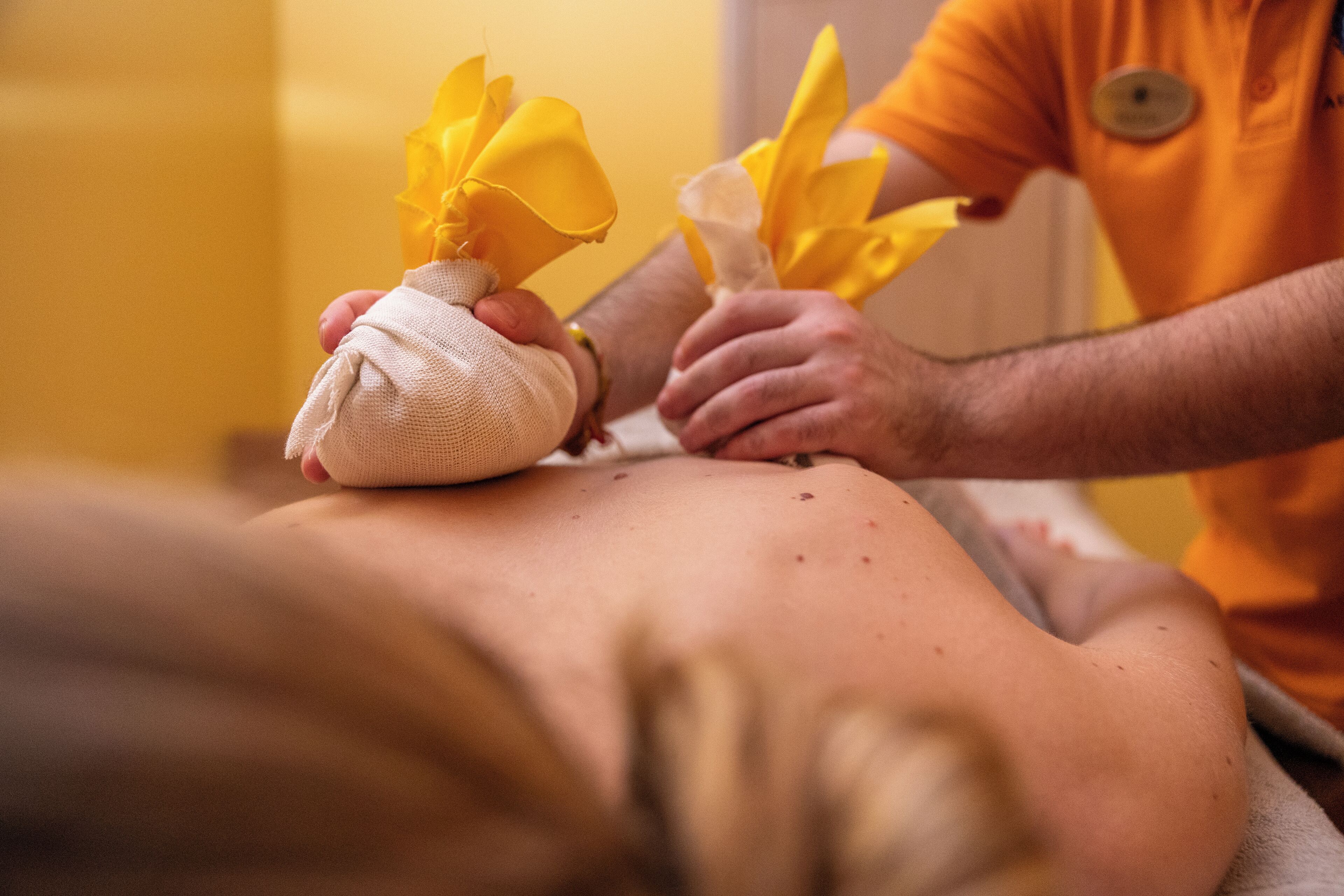 Sesión de masoterapia donde un terapeuta aplica una toalla y flores amarillas en la espalda de un cliente.