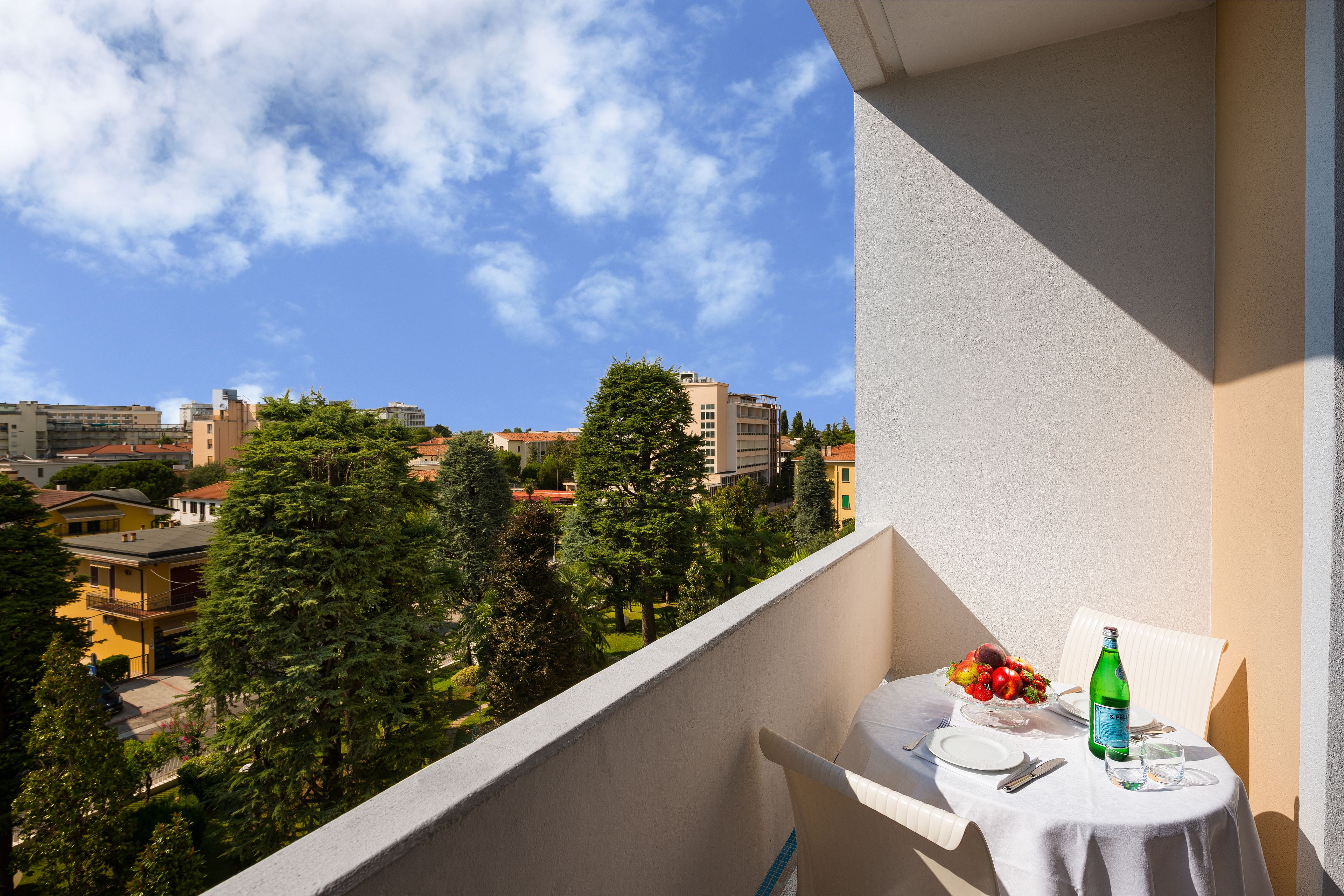 Een balkon met een tafel gedekt voor twee personen, een fles en een schaal fruit.