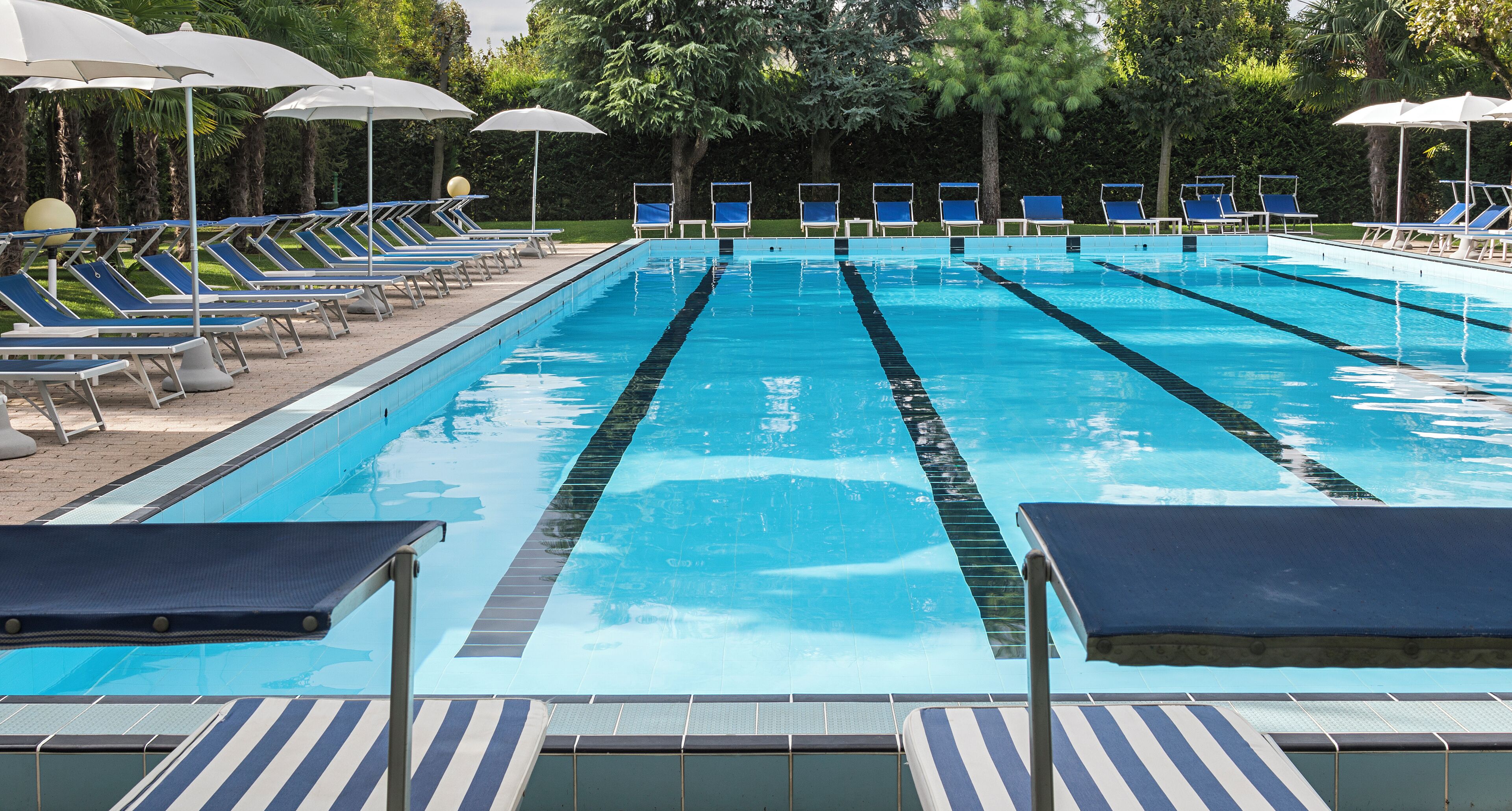 Una piscina con varias pistas, tumbonas y sombrillas.