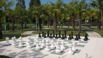 A large outdoor chessboard set up in a park with palm trees and a clear sky.
