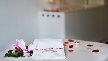 Una toalla blanca doblada con el logotipo 'Romantic Spa', una flor rosa y pétalos de rosa dispersos sobre una mesa.