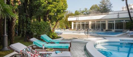 A pool area with lounge chairs and a building with large windows.