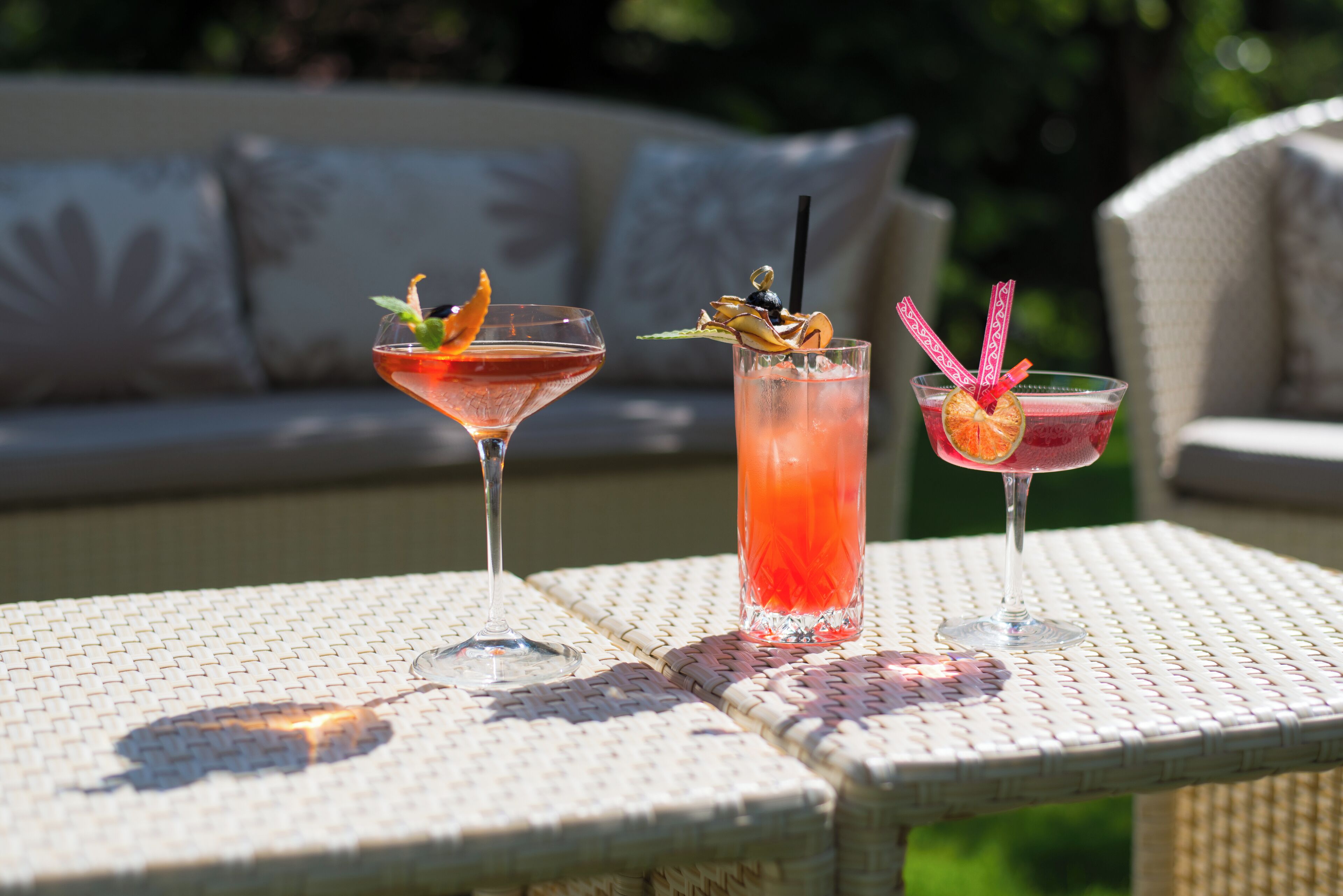 Drei Cocktails auf einem gewebten Tisch, im Hintergrund eine Couch.
