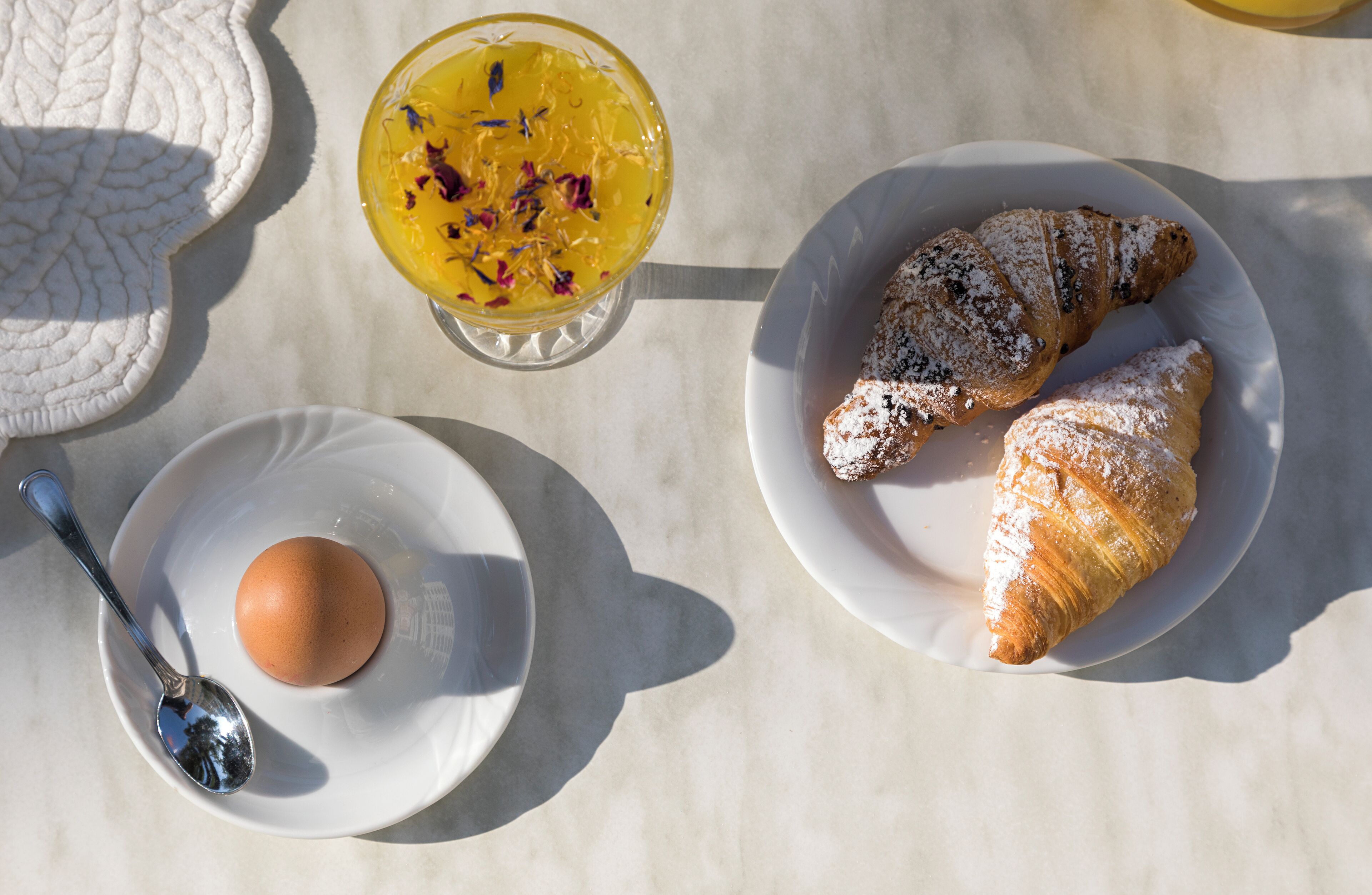 A breakfast setting with a croissant, a bowl of fruit salad, and a boiled egg on a table.