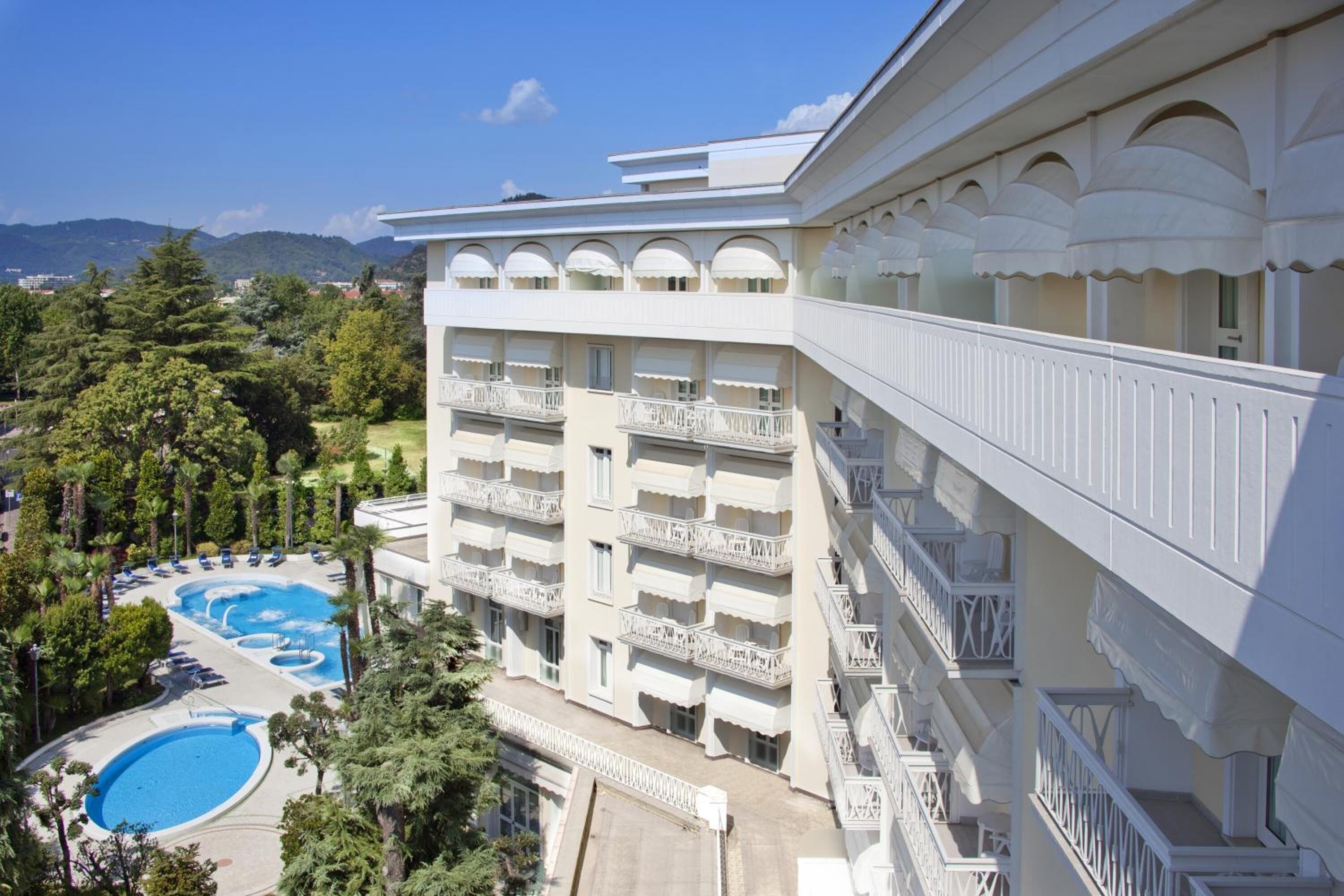 A hotel with multiple balconies, a swimming pool, and a view of the surrounding landscape.