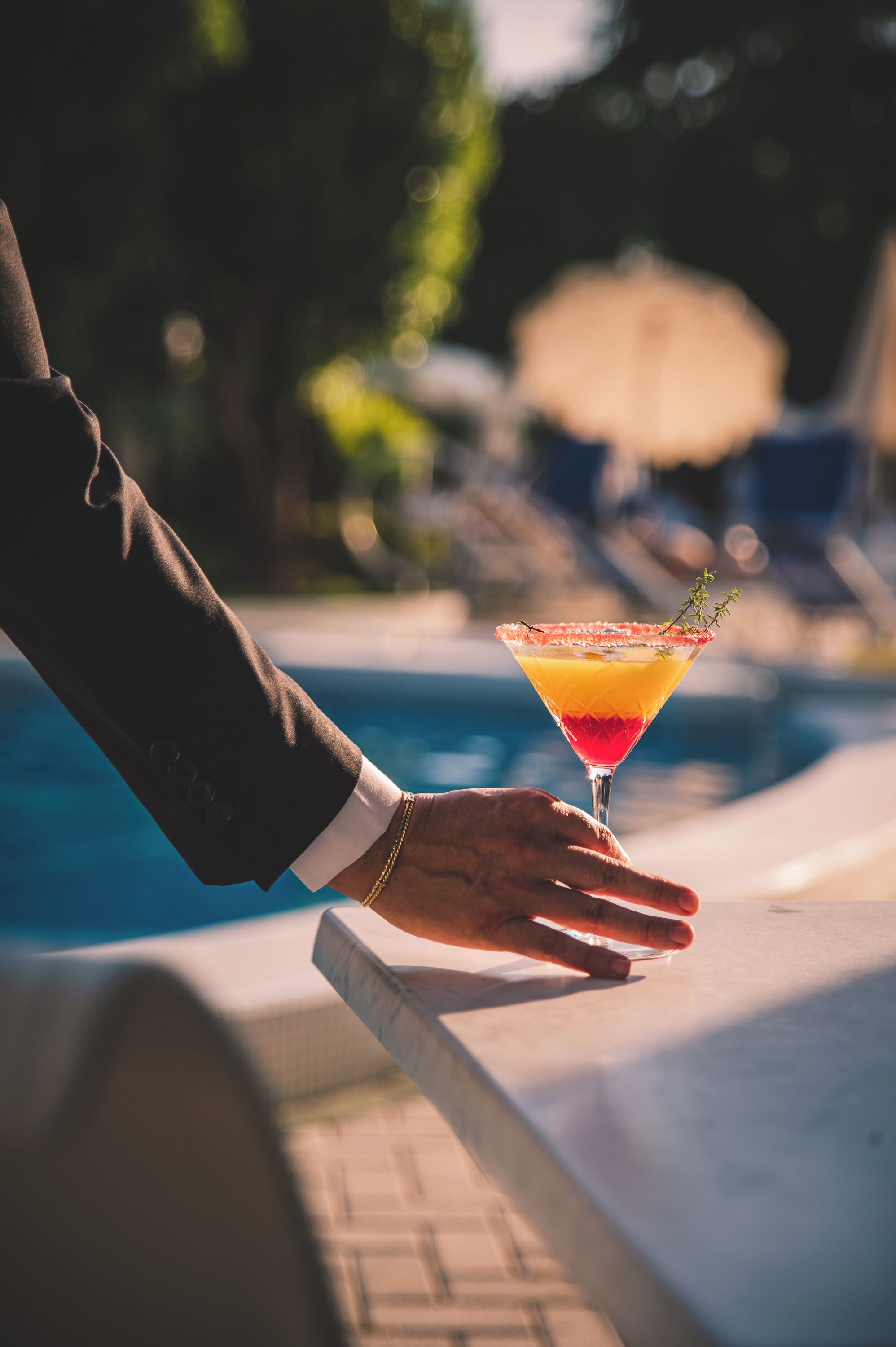 A hand holding a cocktail by a poolside.