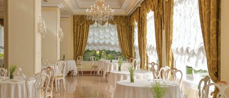 A formal dining room with round tables, white chairs, and gold curtains.