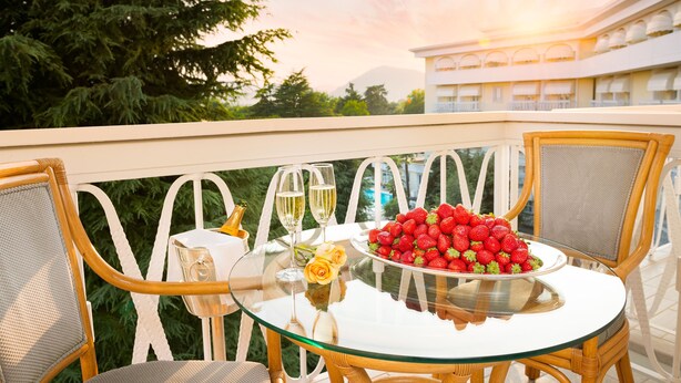 A glass table with two wine glasses, a bowl of strawberries, and a yellow rose on a balcony with wicker chairs. -  HOTEL TERME DUE TORRI - Adults Hideaway & SPA (Abano Terme)