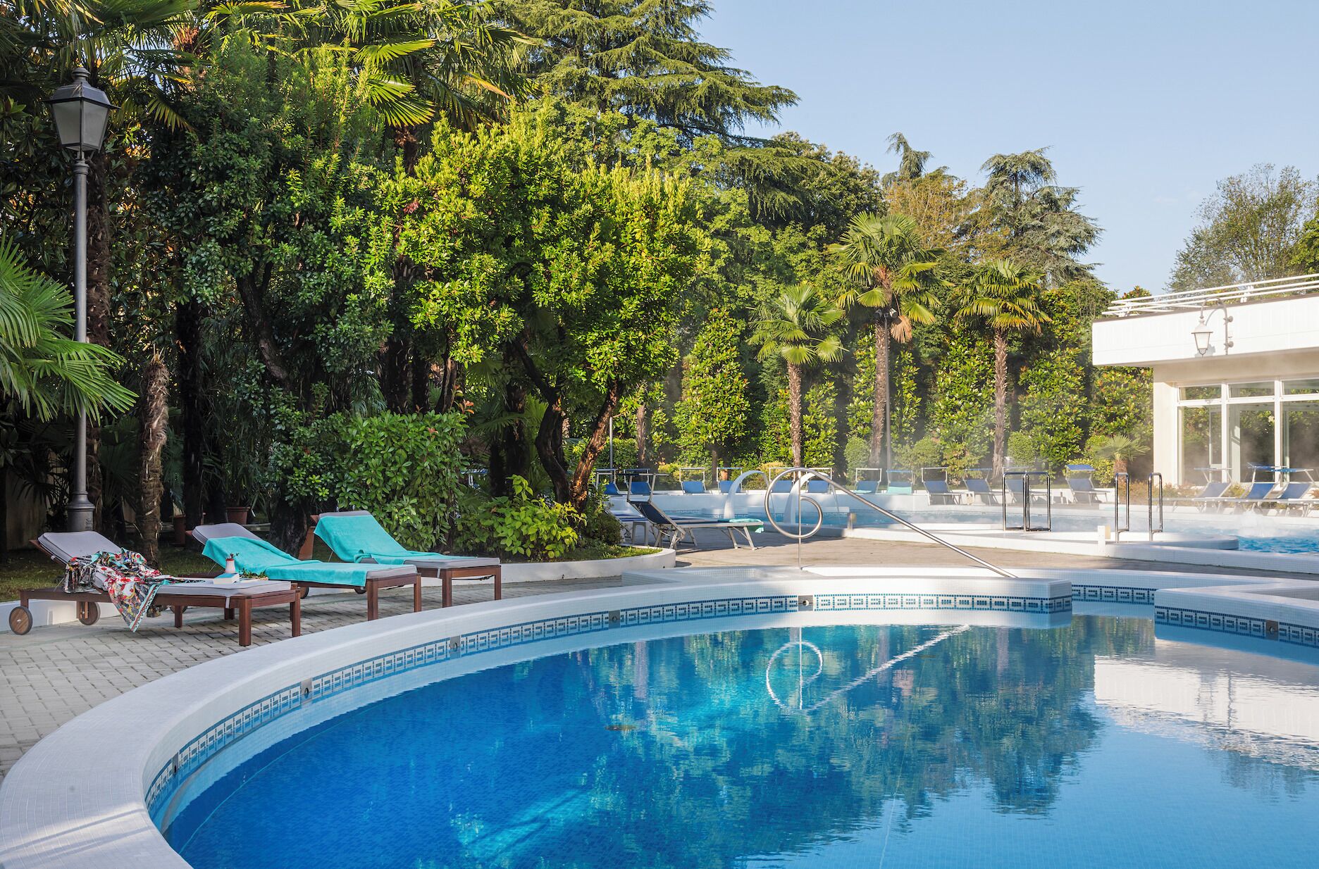 A pool area with lounge chairs and a hot tub, surrounded by lush greenery and trees.