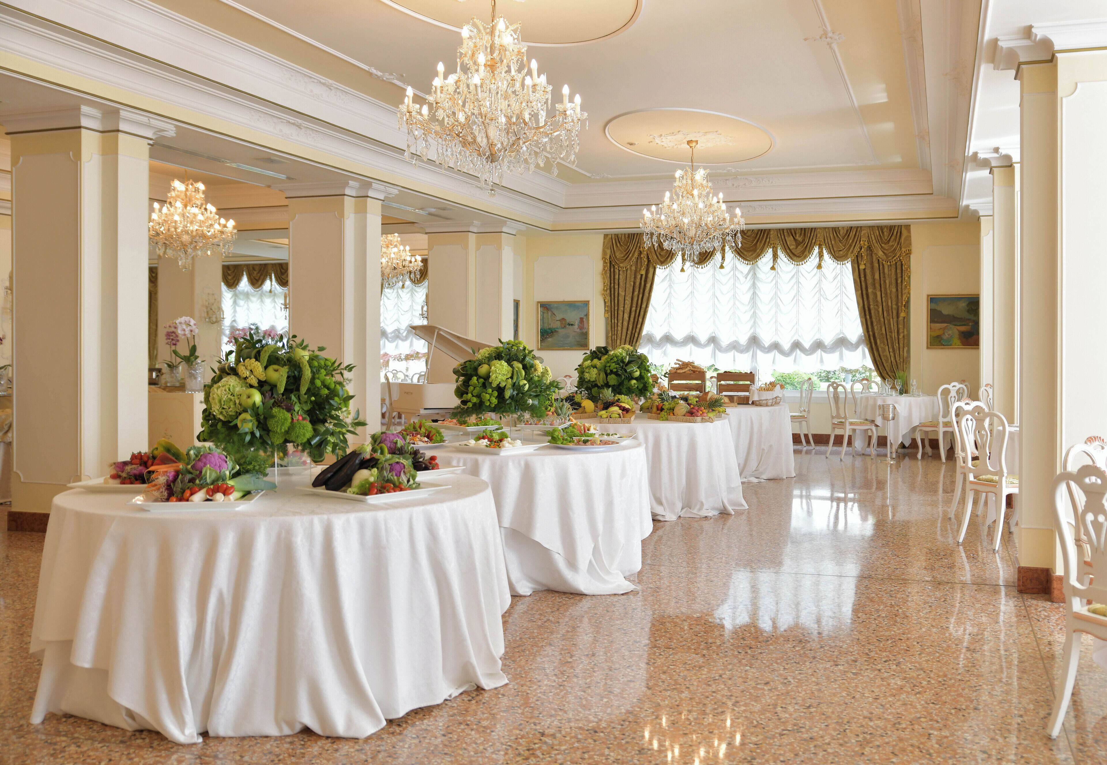 Un amplio salón de banquetes con varias mesas redondas cubiertas con manteles blancos, decoradas con centros de mesa florales.