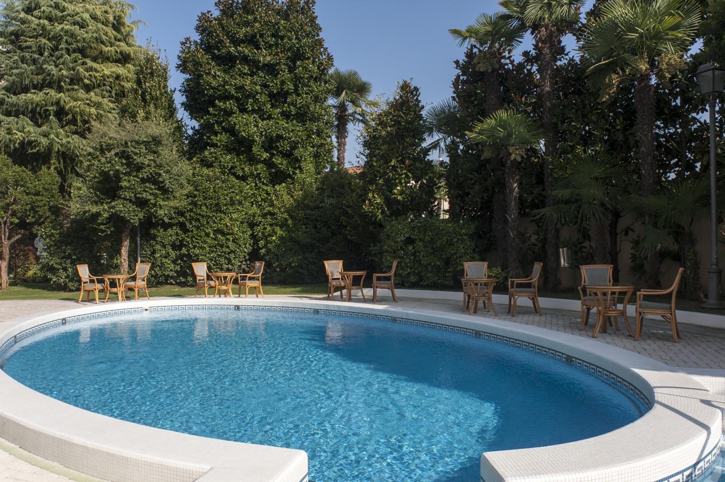 A swimming pool with lounge chairs and tables, surrounded by trees.